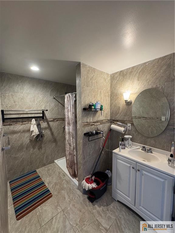 bathroom featuring marble finish floor, tile walls, vanity, and a shower with curtain