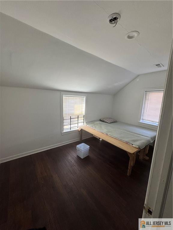 unfurnished bedroom with dark wood-style flooring, visible vents, vaulted ceiling, and baseboards