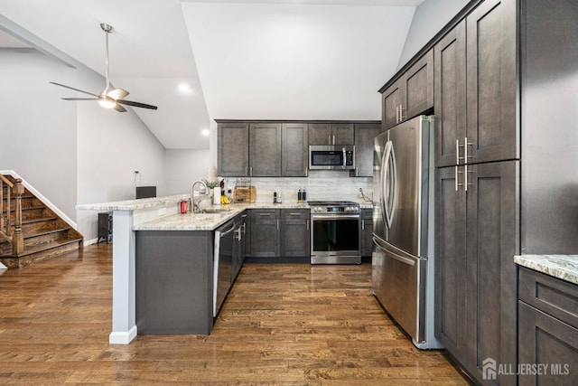 kitchen featuring dark brown cabinetry, appliances with stainless steel finishes, light stone counters, a peninsula, and a sink