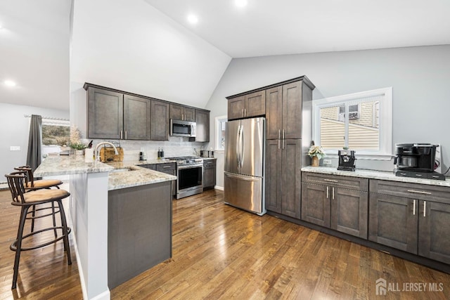 kitchen featuring stainless steel appliances, dark wood-type flooring, a sink, light stone countertops, and a peninsula