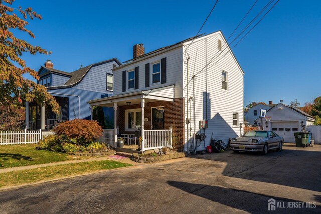 view of front of house with driveway, a chimney, an outbuilding, a porch, and brick siding