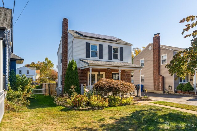 view of front of home featuring brick siding, a chimney, a front yard, roof mounted solar panels, and fence