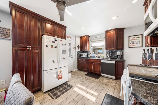 kitchen with white appliances, dark stone counters, decorative backsplash, wood finish floors, and a sink