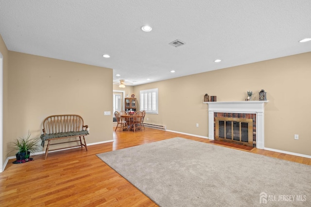 sitting room featuring light wood-type flooring, a brick fireplace, recessed lighting, baseboards, and a baseboard heating unit