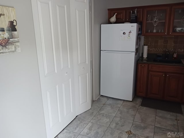 kitchen with decorative backsplash, glass insert cabinets, freestanding refrigerator, light tile patterned flooring, and a sink