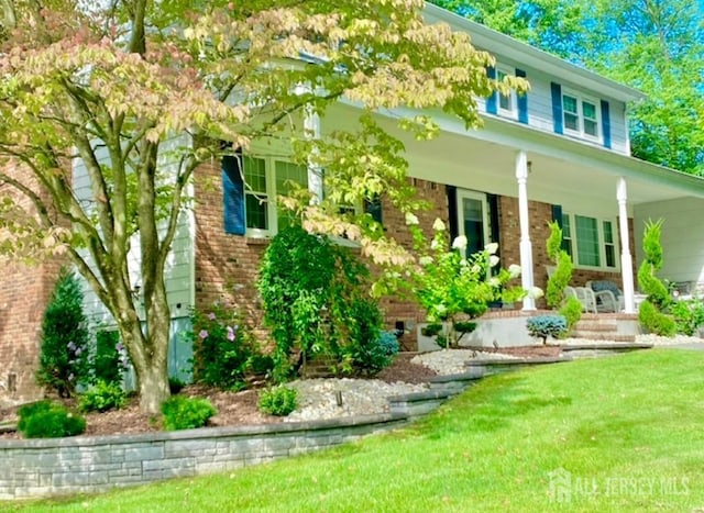 view of front facade featuring brick siding, a porch, and a front lawn