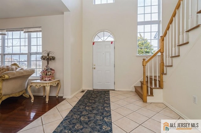 entryway with light tile patterned floors, stairs, baseboards, and a wealth of natural light