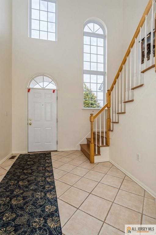 entrance foyer featuring a towering ceiling, light tile patterned floors, stairs, and baseboards