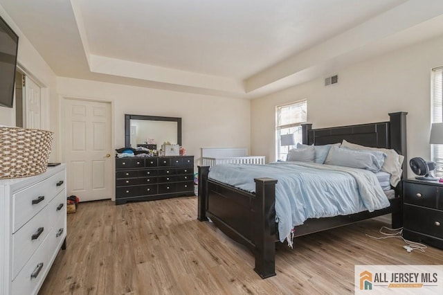 bedroom featuring a tray ceiling, visible vents, and light wood finished floors