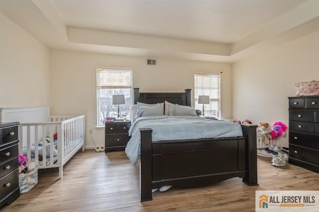 bedroom featuring a raised ceiling, visible vents, and wood finished floors