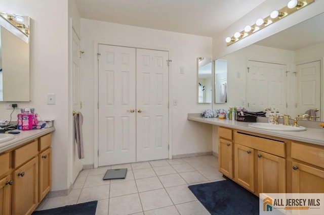 bathroom with a closet, two vanities, tile patterned flooring, and a sink