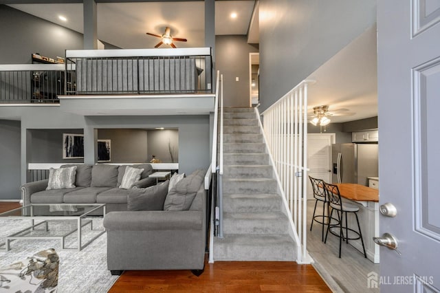 living room with ceiling fan, a high ceiling, wood finished floors, and stairs