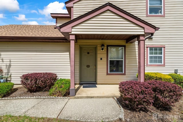 doorway to property featuring covered porch and roof with shingles