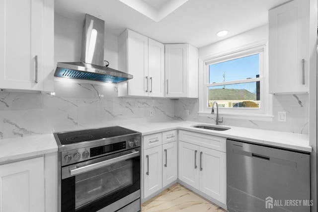 kitchen featuring sink, light stone counters, appliances with stainless steel finishes, wall chimney range hood, and white cabinets