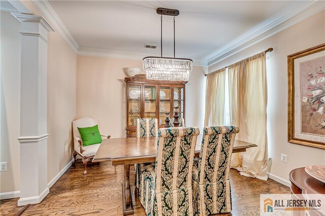 dining room featuring wood finished floors, visible vents, baseboards, decorative columns, and crown molding