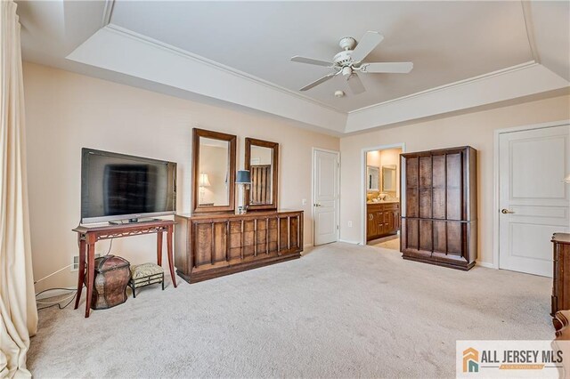 bedroom featuring a tray ceiling, light colored carpet, connected bathroom, ceiling fan, and baseboards