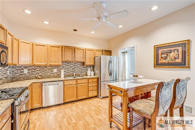 kitchen with light stone countertops, a sink, appliances with stainless steel finishes, light wood-type flooring, and decorative backsplash