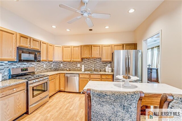 kitchen featuring decorative backsplash, light stone countertops, stainless steel appliances, light wood-style floors, and a sink