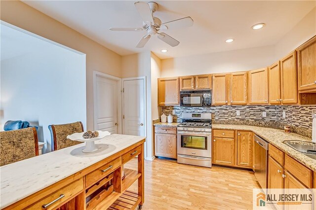 kitchen with stainless steel appliances, light stone counters, light wood-style flooring, and decorative backsplash