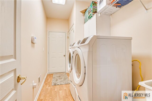 clothes washing area featuring laundry area, light wood-type flooring, washing machine and dryer, and baseboards