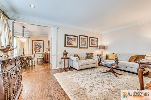 living area with baseboards, wood finished floors, decorative columns, and crown molding