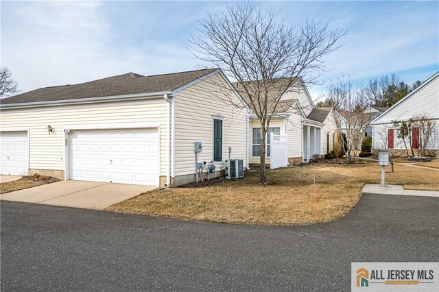 view of property exterior featuring driveway, a lawn, roof with shingles, an attached garage, and central air condition unit