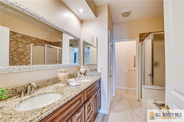 bathroom with double vanity, a stall shower, a sink, and baseboards