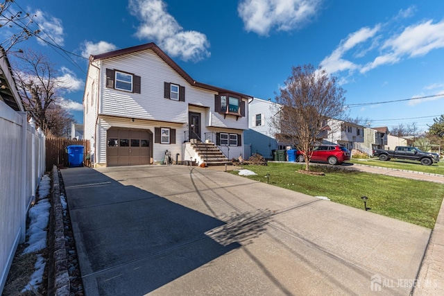 bi-level home featuring concrete driveway, fence, a front lawn, and an attached garage