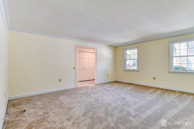 carpeted spare room with crown molding, baseboards, and a healthy amount of sunlight