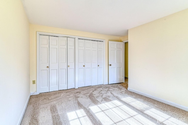 unfurnished bedroom featuring carpet floors, multiple closets, and baseboards