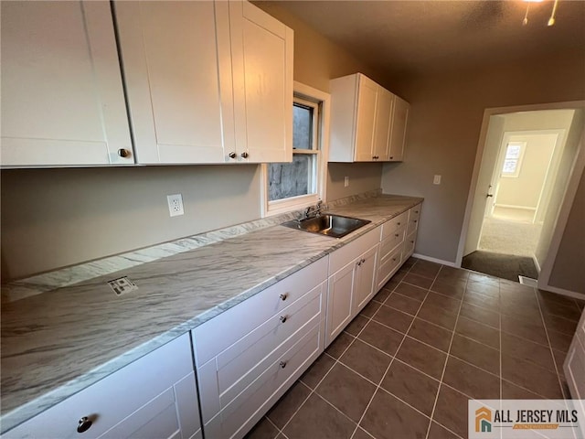 kitchen with light countertops, a sink, baseboards, dark tile patterned flooring, and white cabinetry