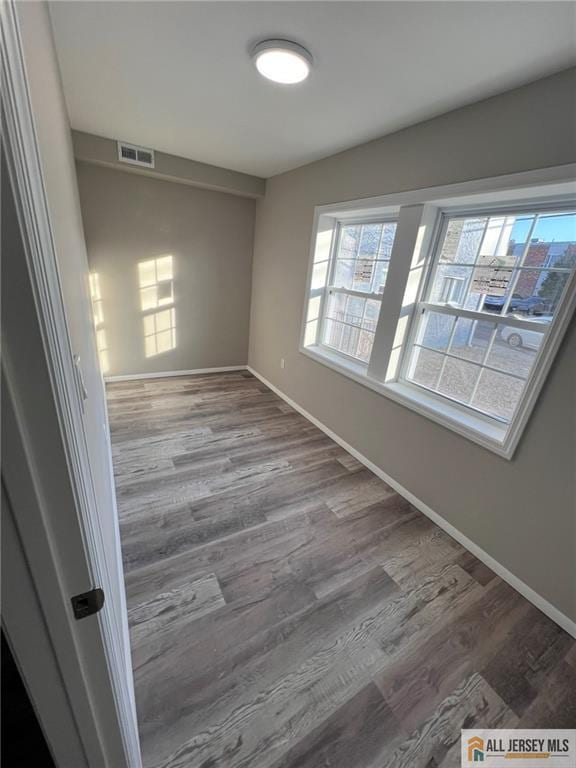 empty room featuring baseboards, wood finished floors, and visible vents