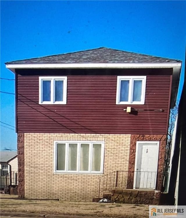 exterior space featuring brick siding and roof with shingles