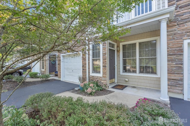 doorway to property featuring driveway, stone siding, and a garage