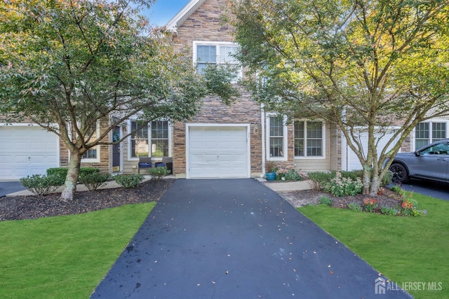 view of property hidden behind natural elements with stone siding, a front yard, and driveway