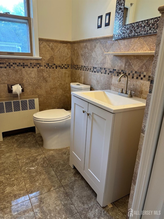 bathroom with tile walls, radiator, vanity, and toilet