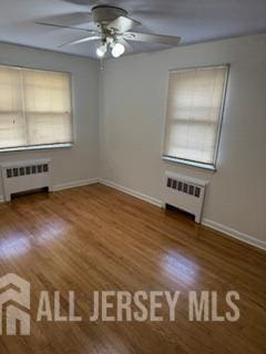 spare room featuring hardwood / wood-style floors, radiator heating unit, and ceiling fan