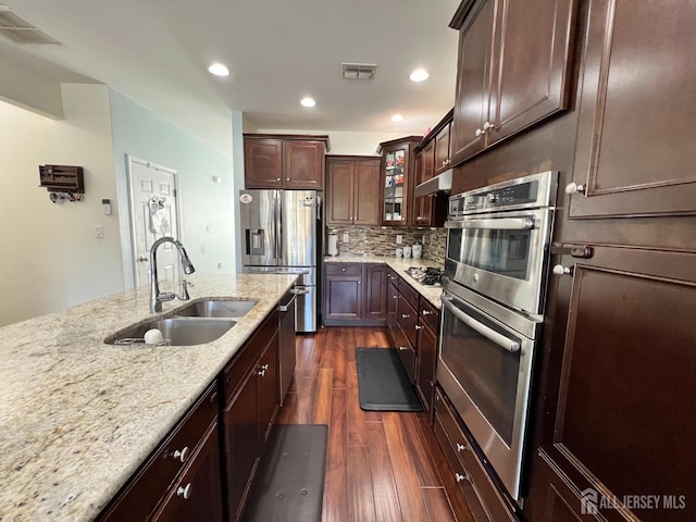 kitchen featuring light stone countertops, sink, dark hardwood / wood-style floors, backsplash, and appliances with stainless steel finishes