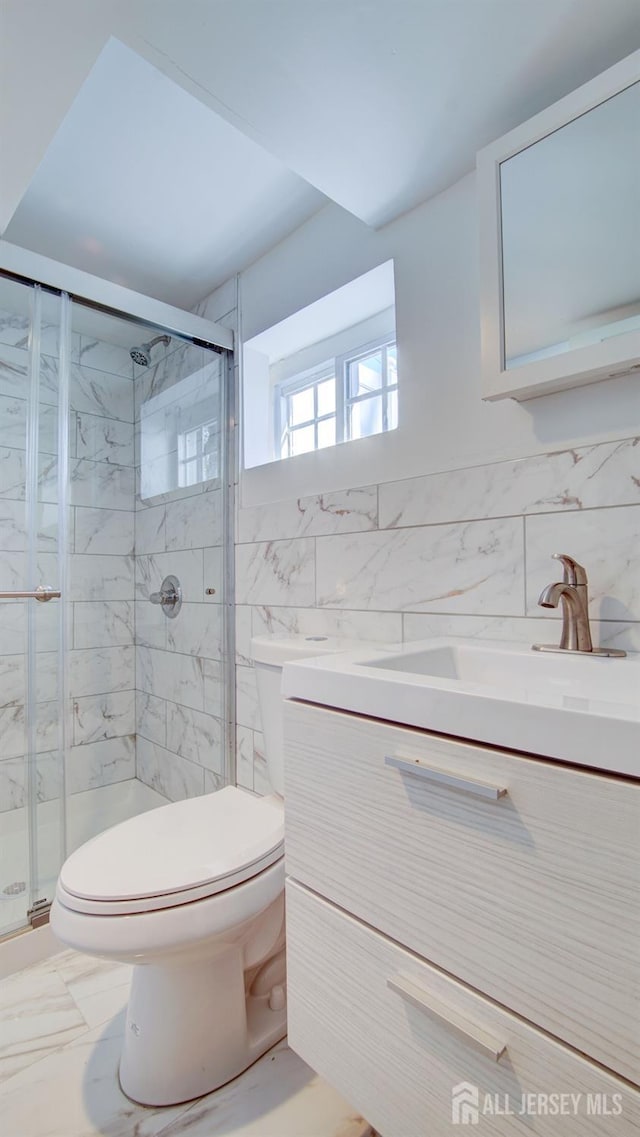 bathroom featuring tile walls, toilet, a stall shower, vanity, and marble finish floors