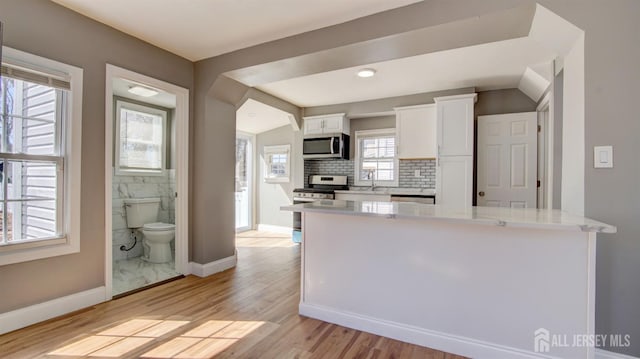 kitchen with light wood-type flooring, white cabinetry, backsplash, baseboards, and appliances with stainless steel finishes