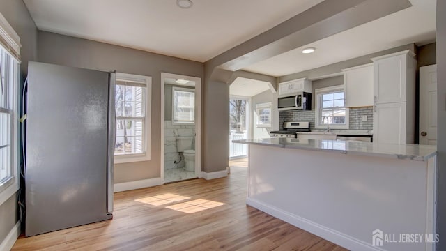 kitchen featuring appliances with stainless steel finishes, baseboards, white cabinetry, backsplash, and light wood-style floors