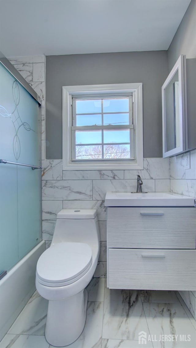 full bathroom featuring marble look tile flooring, vanity, tile walls, toilet, and wainscoting