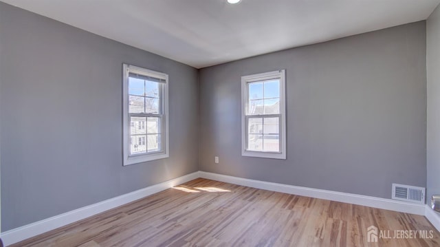 empty room featuring light wood finished floors, baseboards, and visible vents