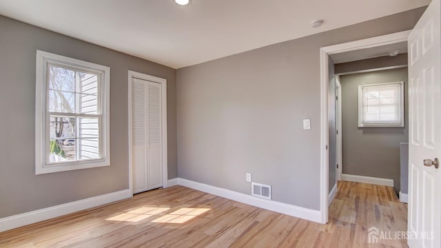 unfurnished bedroom featuring baseboards, multiple windows, light wood finished floors, and visible vents