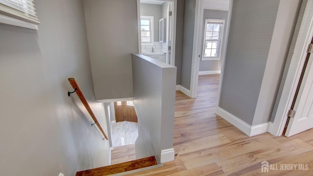 hall featuring an upstairs landing, baseboards, and light wood-style flooring