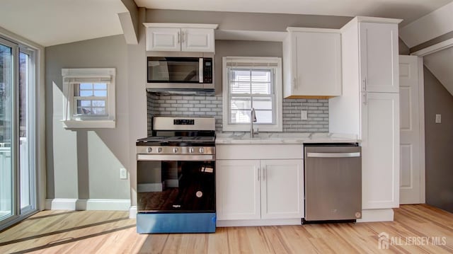 kitchen with appliances with stainless steel finishes, light wood-style flooring, lofted ceiling, and a sink