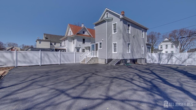 back of property with fence, a gate, a chimney, and central air condition unit
