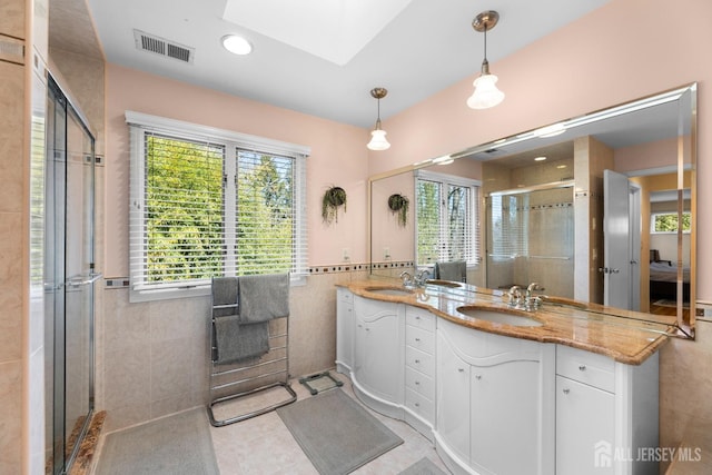 ensuite bathroom with plenty of natural light, tile walls, a stall shower, tile patterned flooring, and double vanity