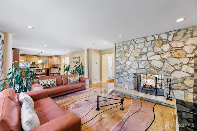living room featuring recessed lighting, a stone fireplace, ornate columns, light wood-style flooring, and baseboards