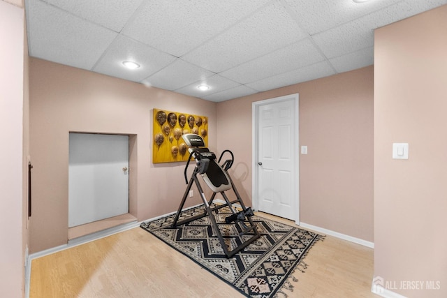 exercise area featuring a paneled ceiling, recessed lighting, baseboards, and wood finished floors